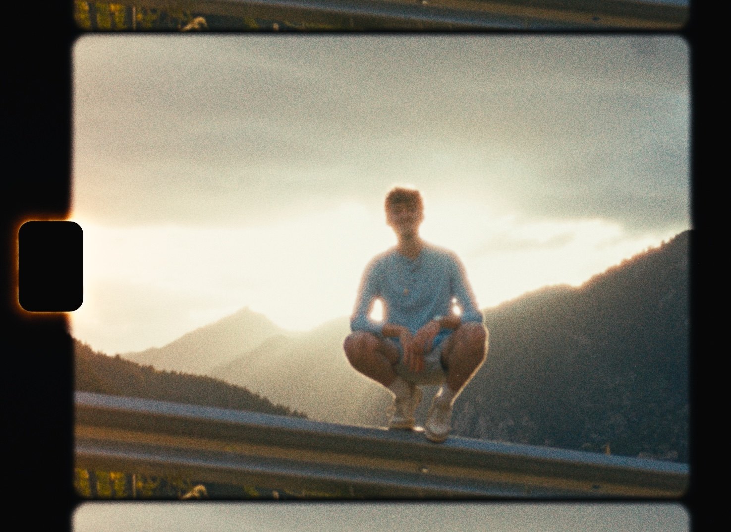 An 8mm frame in the film gate: the sprocket perforation with light blooming through it, rounded gate corners, and neighboring frames visible above and below.