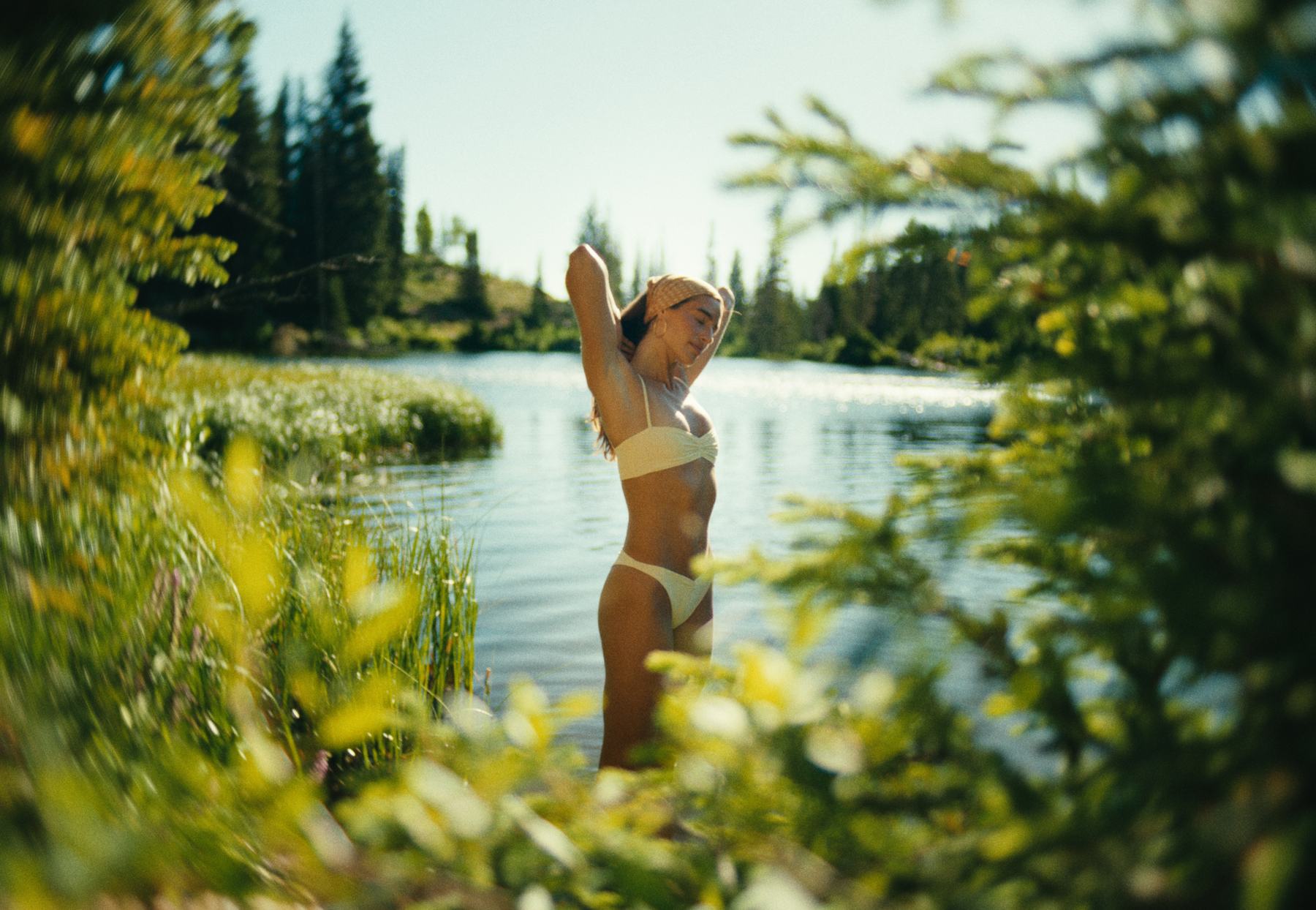 A woman standing in a lake, framed through foliage, the edges swirling around her.